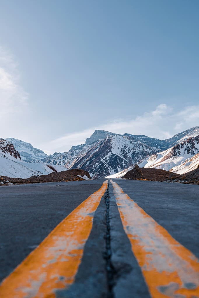 Empty asphalt road with double yellow lines stretching toward snow-capped Andes peaks under a clear blue sky