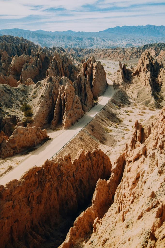 Dirt road winding through ochre rock fins in an arid Argentine canyon under a pale blue sky